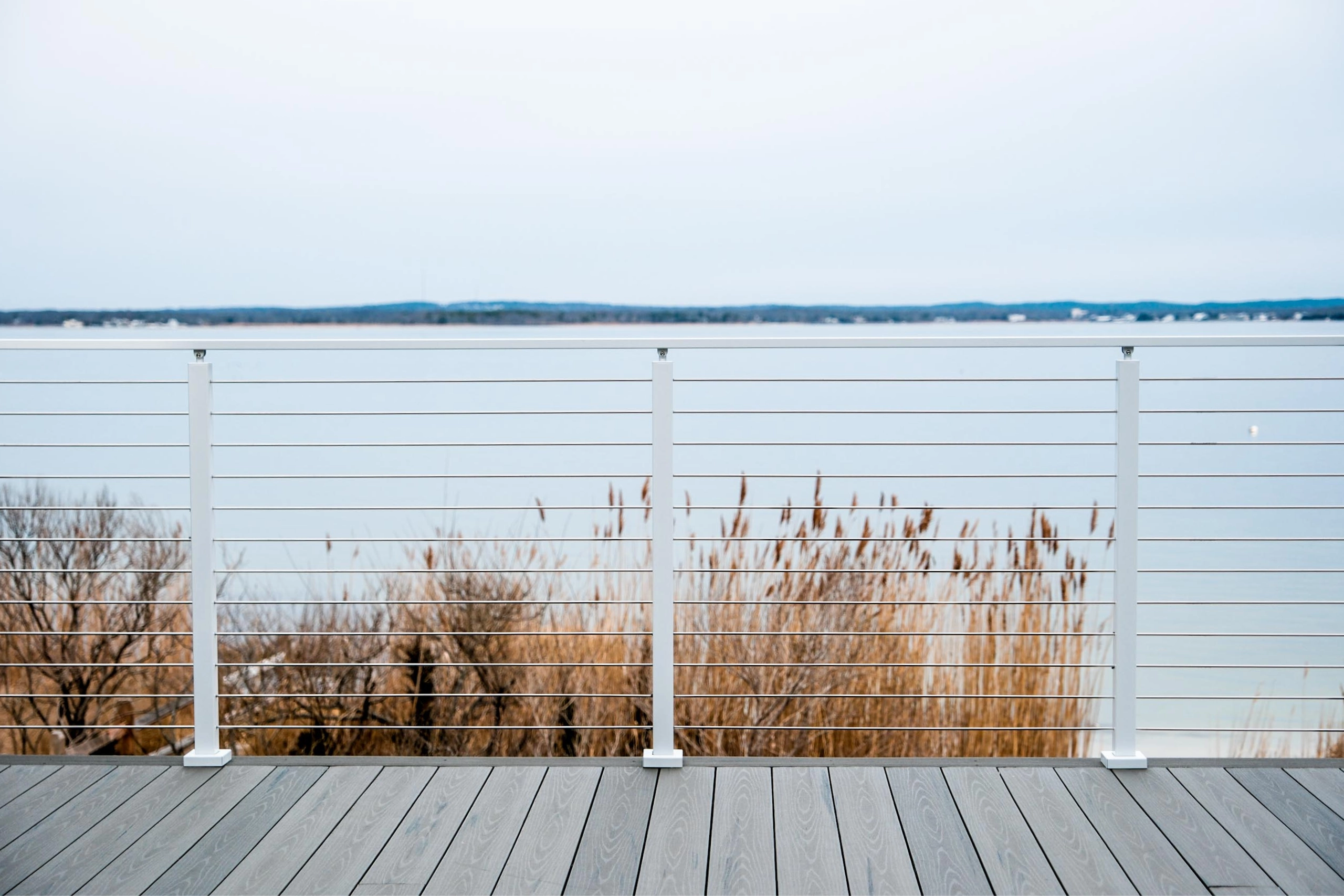 Reeds and grey water beyond a white Signature Rod railing on a weathered deck