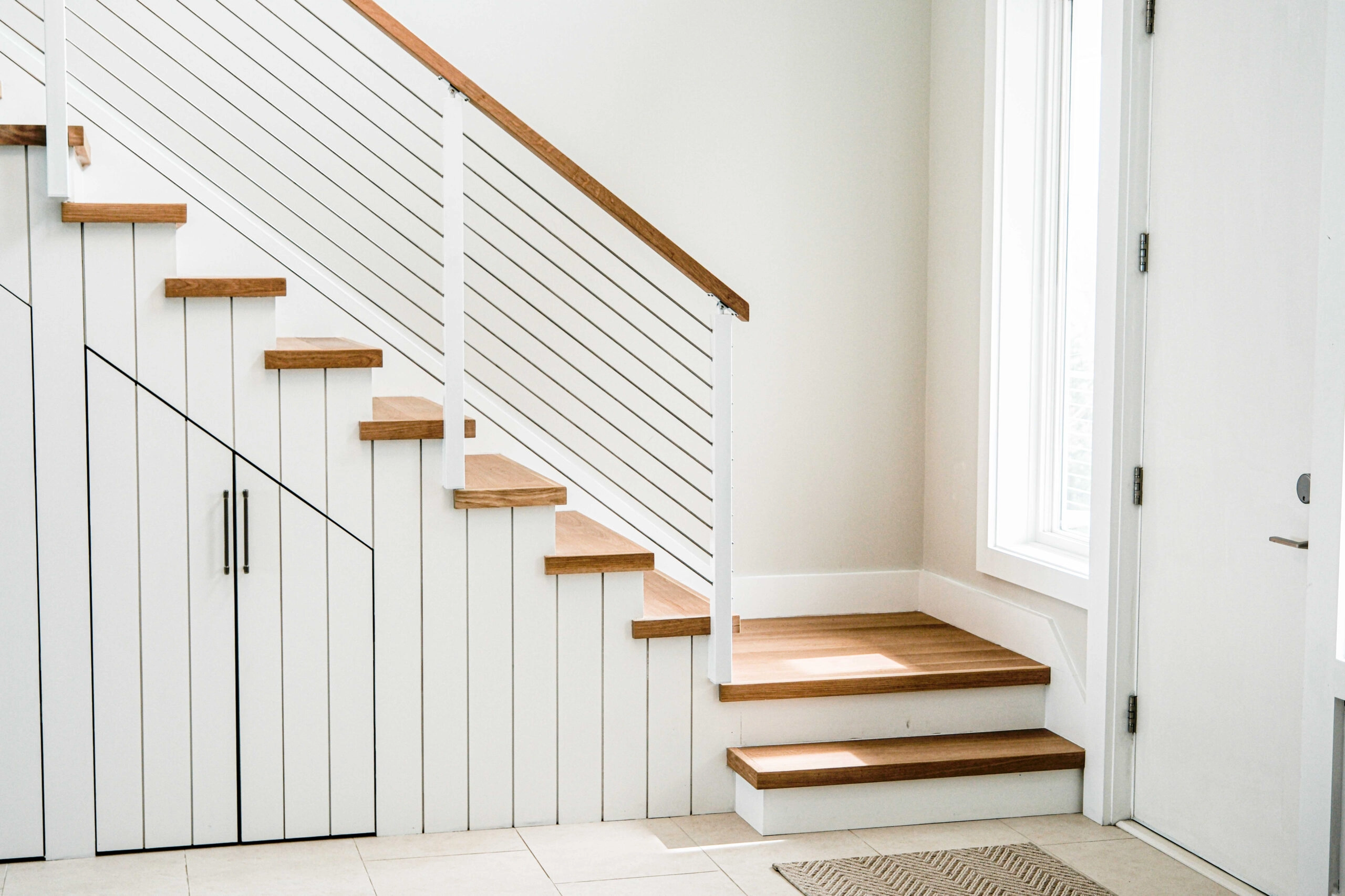 White shiplap under a stair railed in Signature Rod, wood handrail to the entry