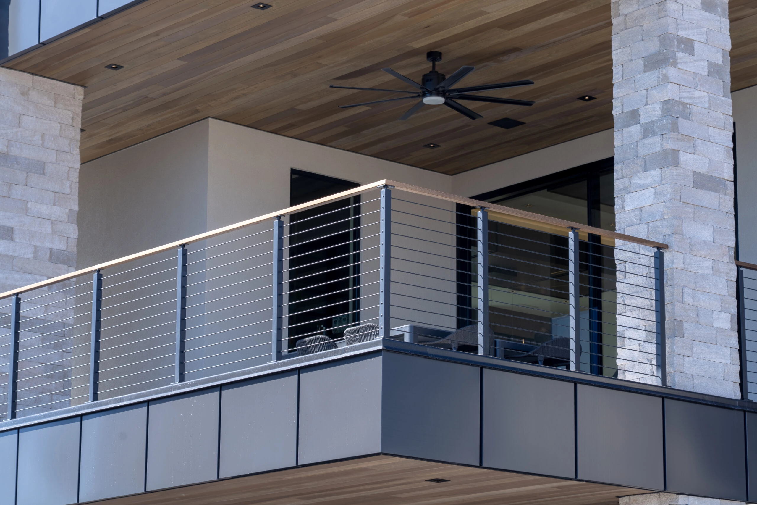 A ceiling fan under a wood-clad porch, stainless Signature Cable railing along the balcony