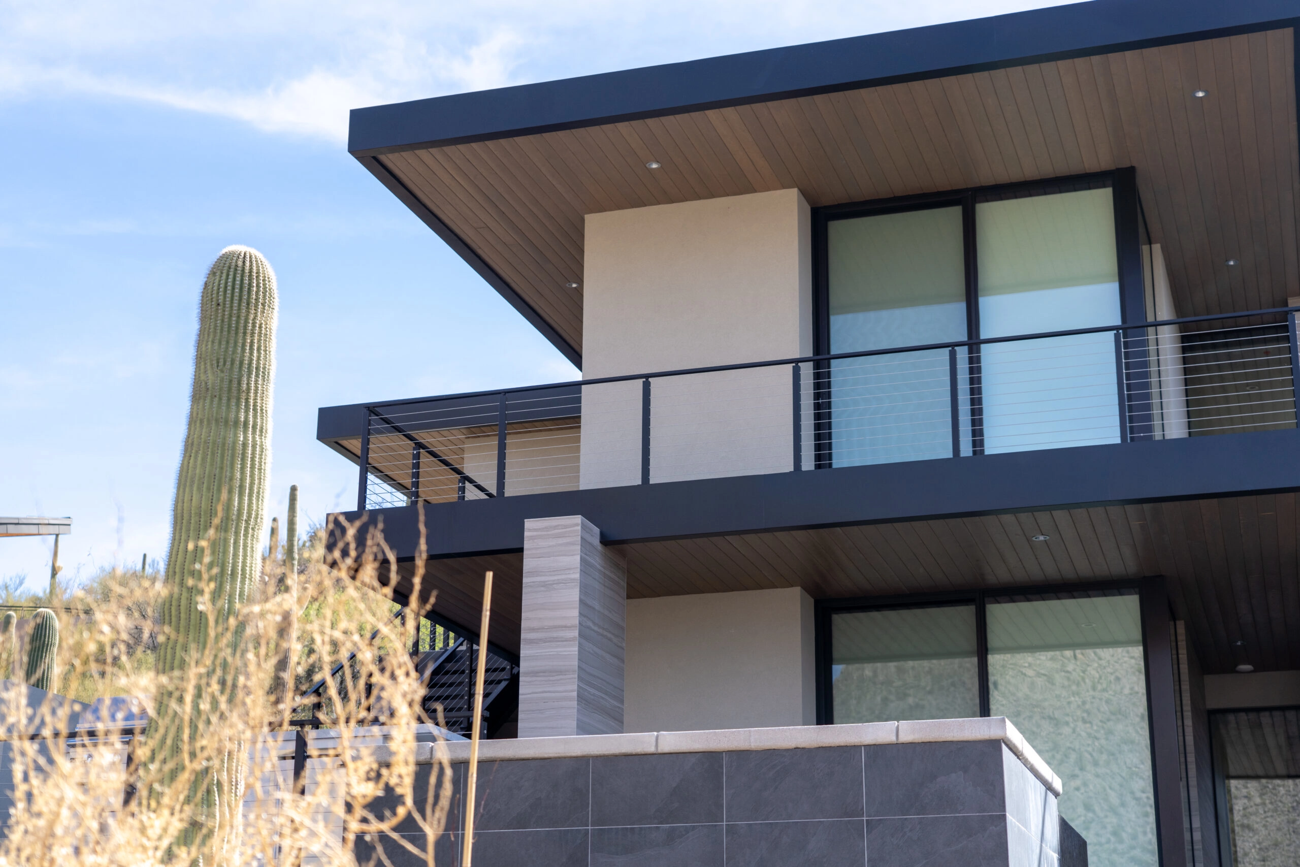 A flat-roofed desert house beside a saguaro; Signature Cable railing edges its balcony