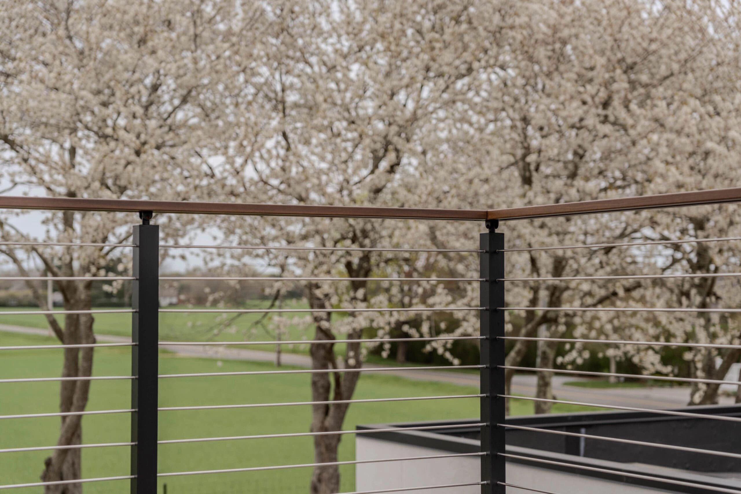 Signature Rod infill spans black posts under a wood top rail, blossoming trees behind