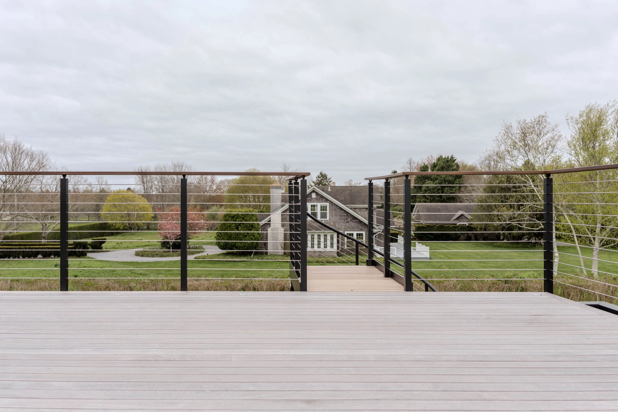 A deck ringed in Signature Rod railing - stainless rods, black posts - overlooks gardens and a house