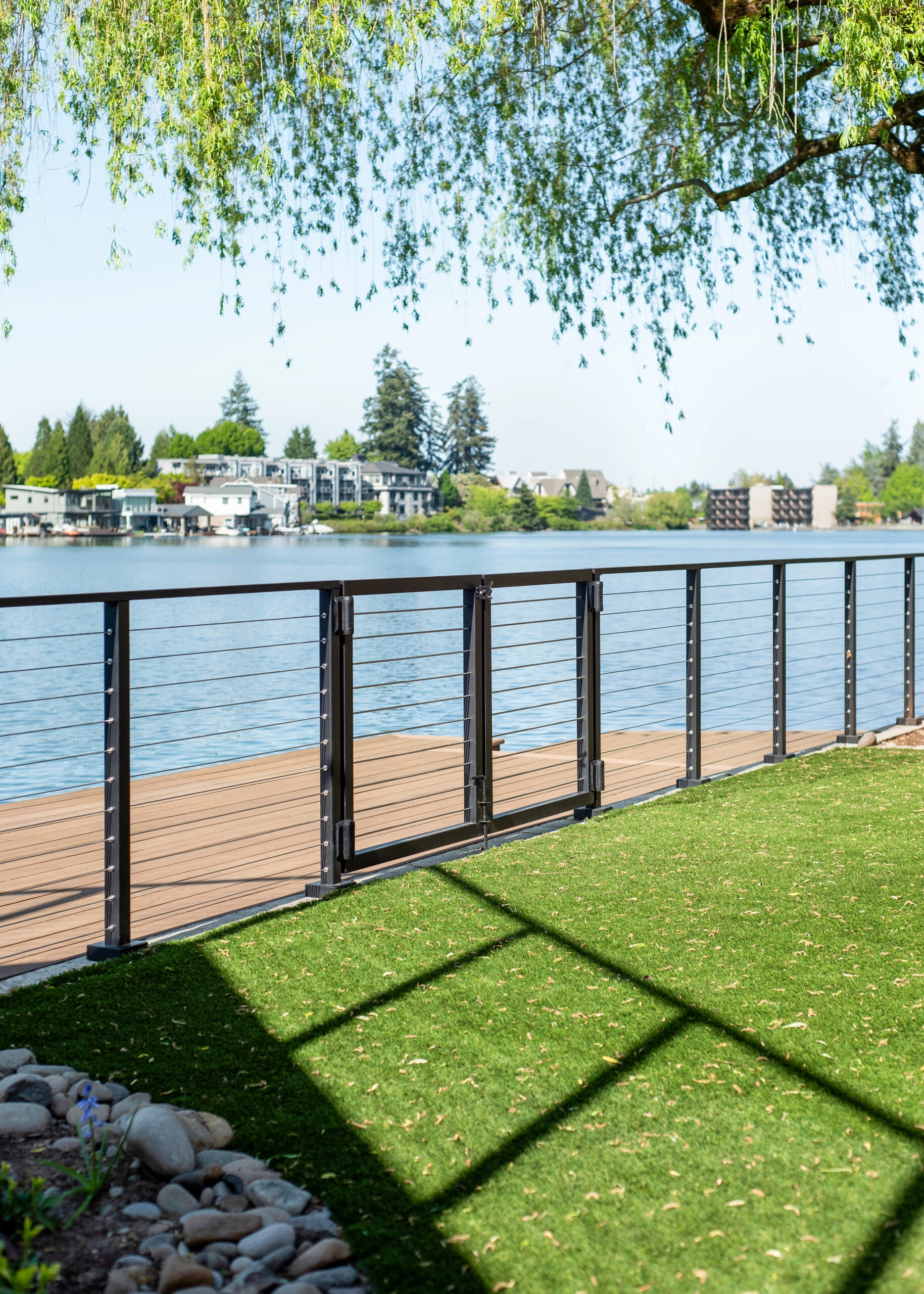 A gate in black Signature Cable railing separates lawn from a lakeside deck