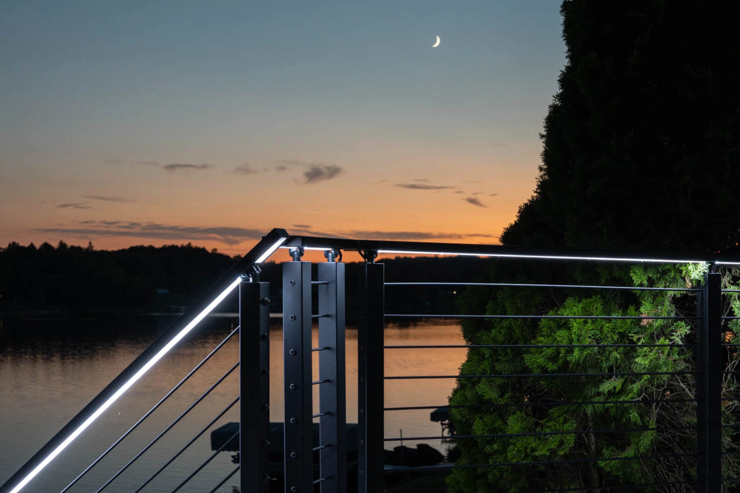 A crescent moon over the lake above lit Signature Rod handrails at dusk