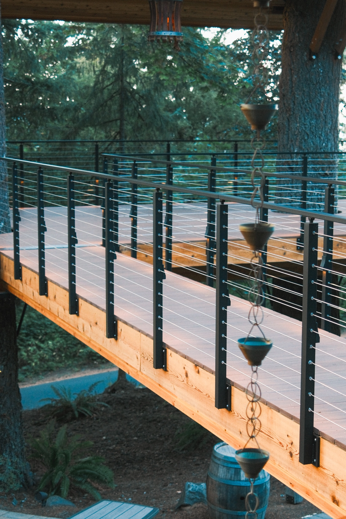 A rain chain hangs beside an elevated wood walkway lined with black Signature Cable railing