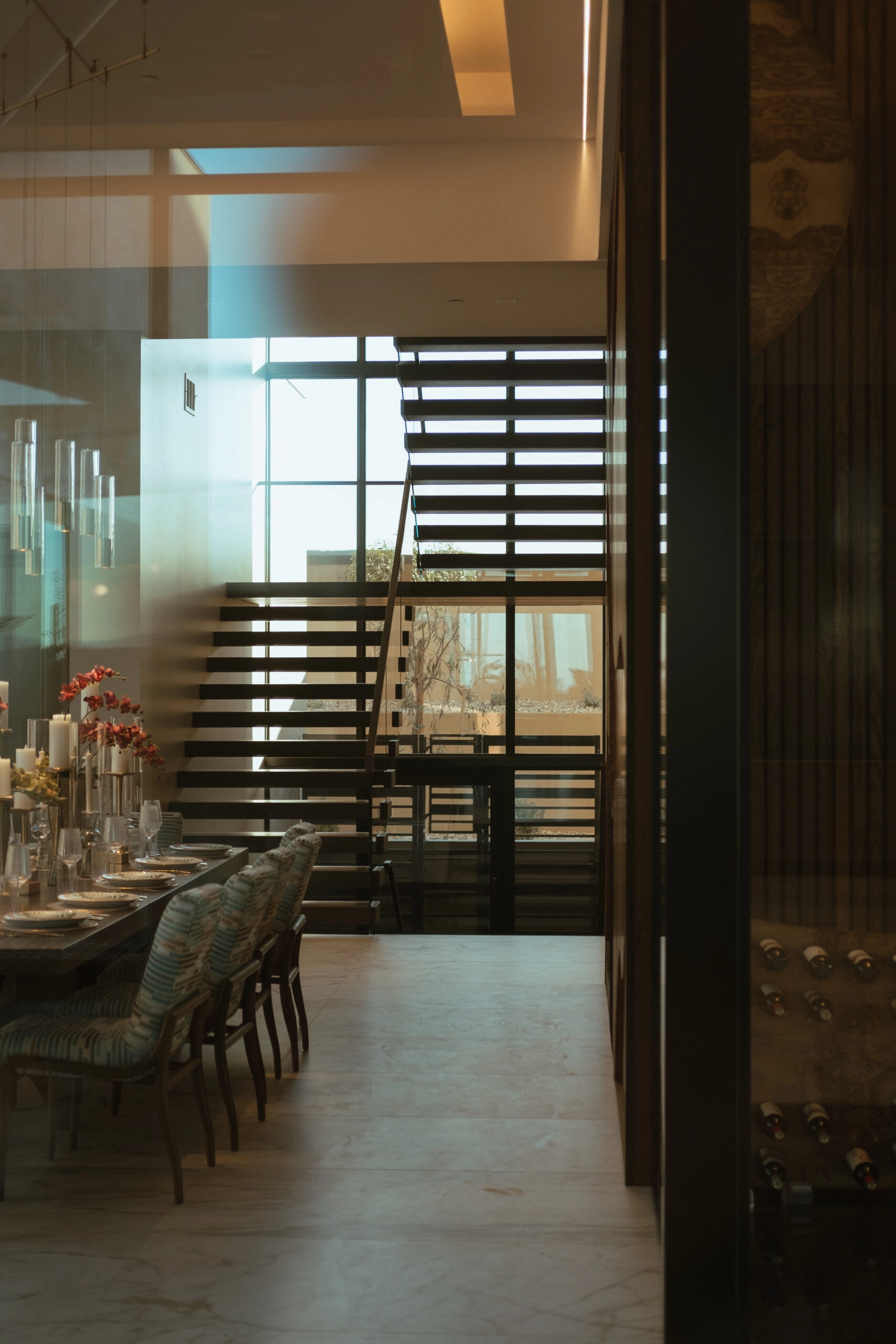 A set dining table with a dark FLIGHT Cantilever stair rising beyond a glass partition