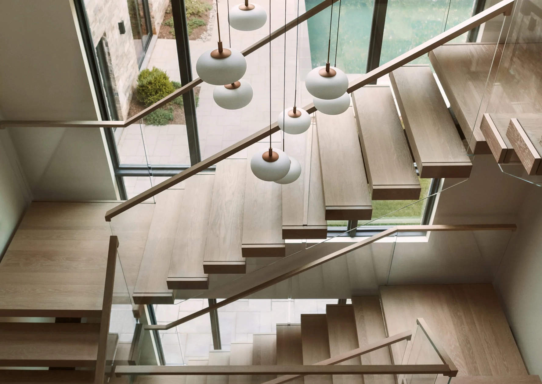 Pendant lights hang above a FLIGHT Mono switchback staircase with pale wood treads and a glass railing