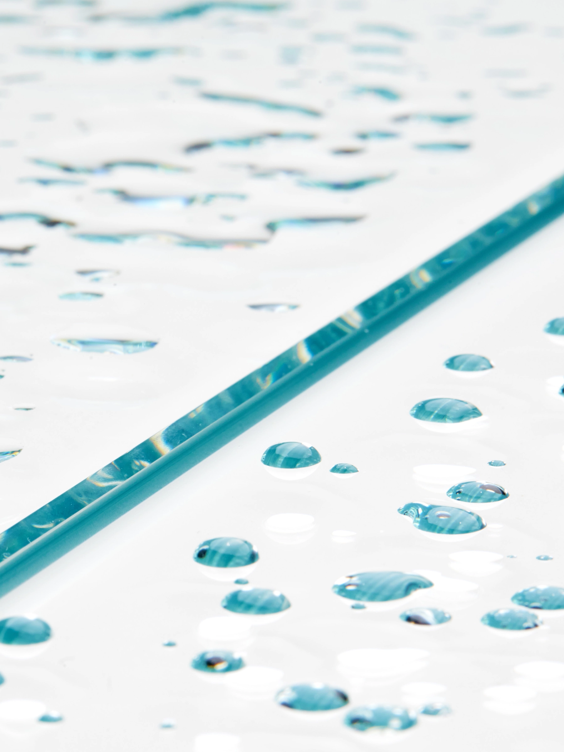Water beads on a glass panel, its polished edge showing green through the pane