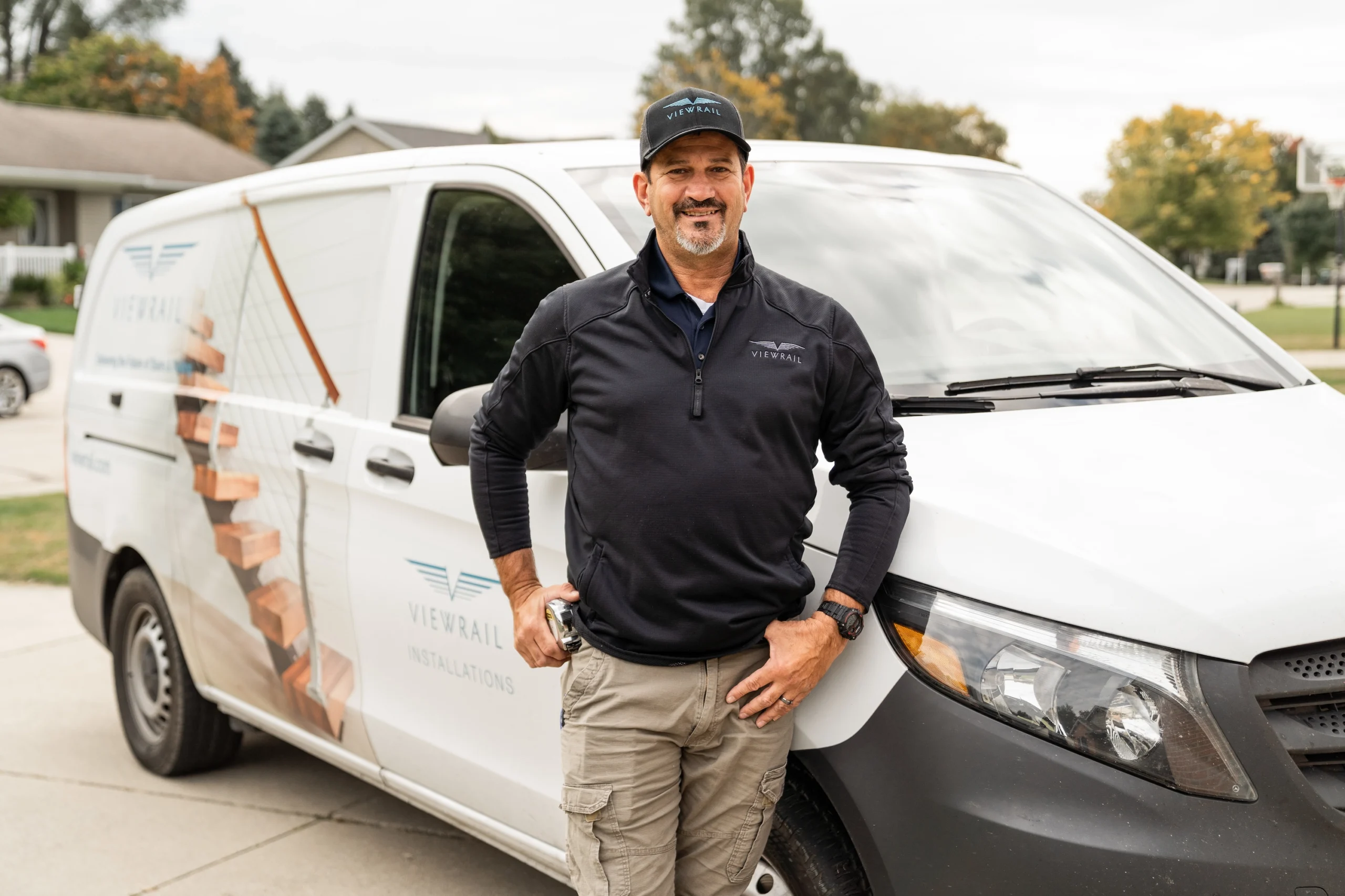Beside a white Viewrail van printed with a floating stair, an installer stands on a driveway