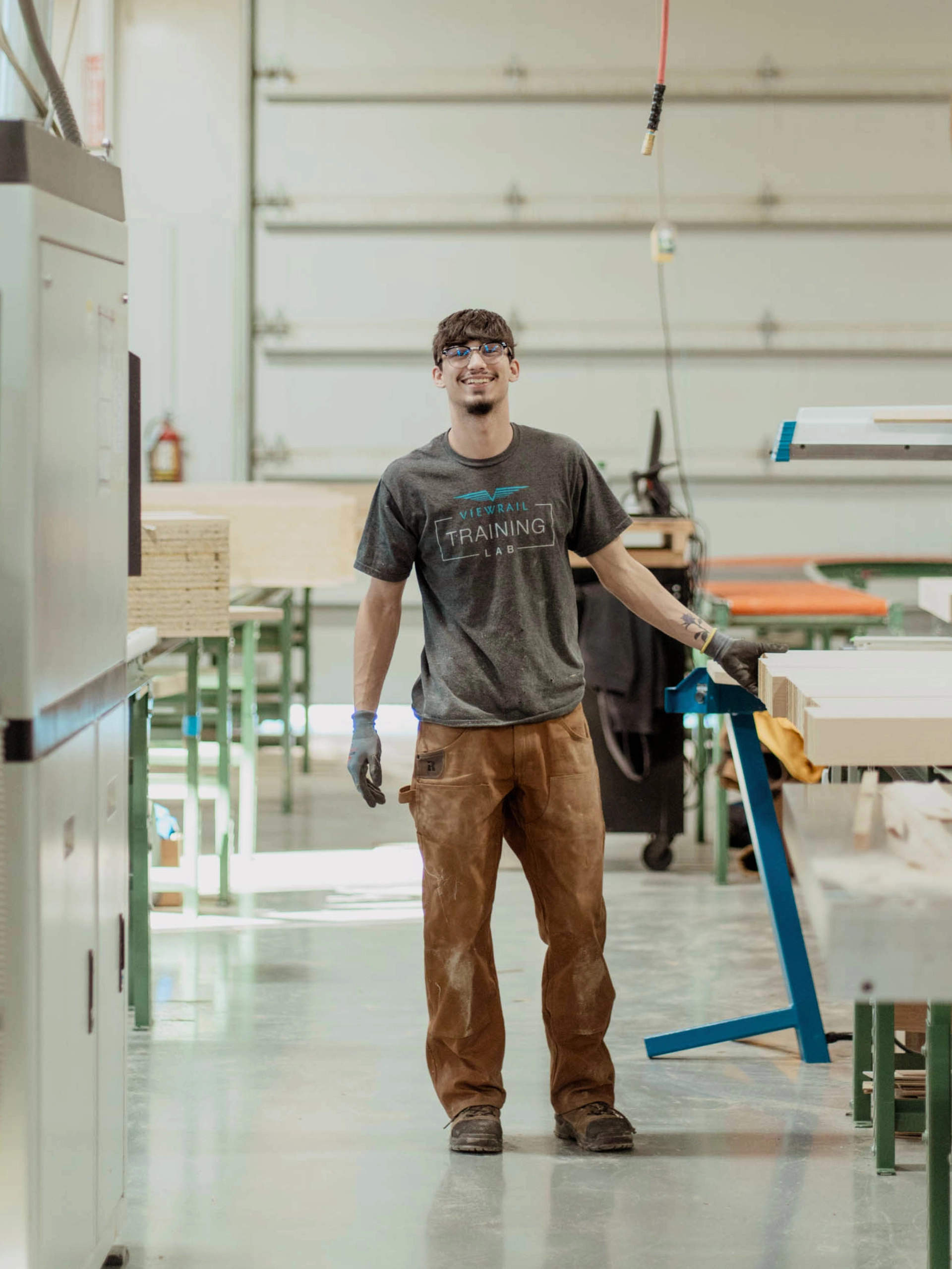 A Viewrail Training Lab installer in safety glasses and gloves stands in a workshop