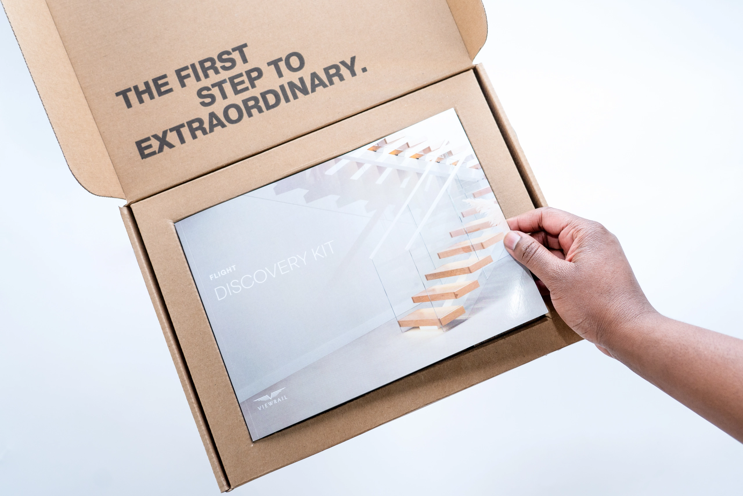 A hand holding a booklet titled 'Flight Discovery Kit' above an open cardboard box with the text 'The first step to extraordinary.' printed inside the lid.