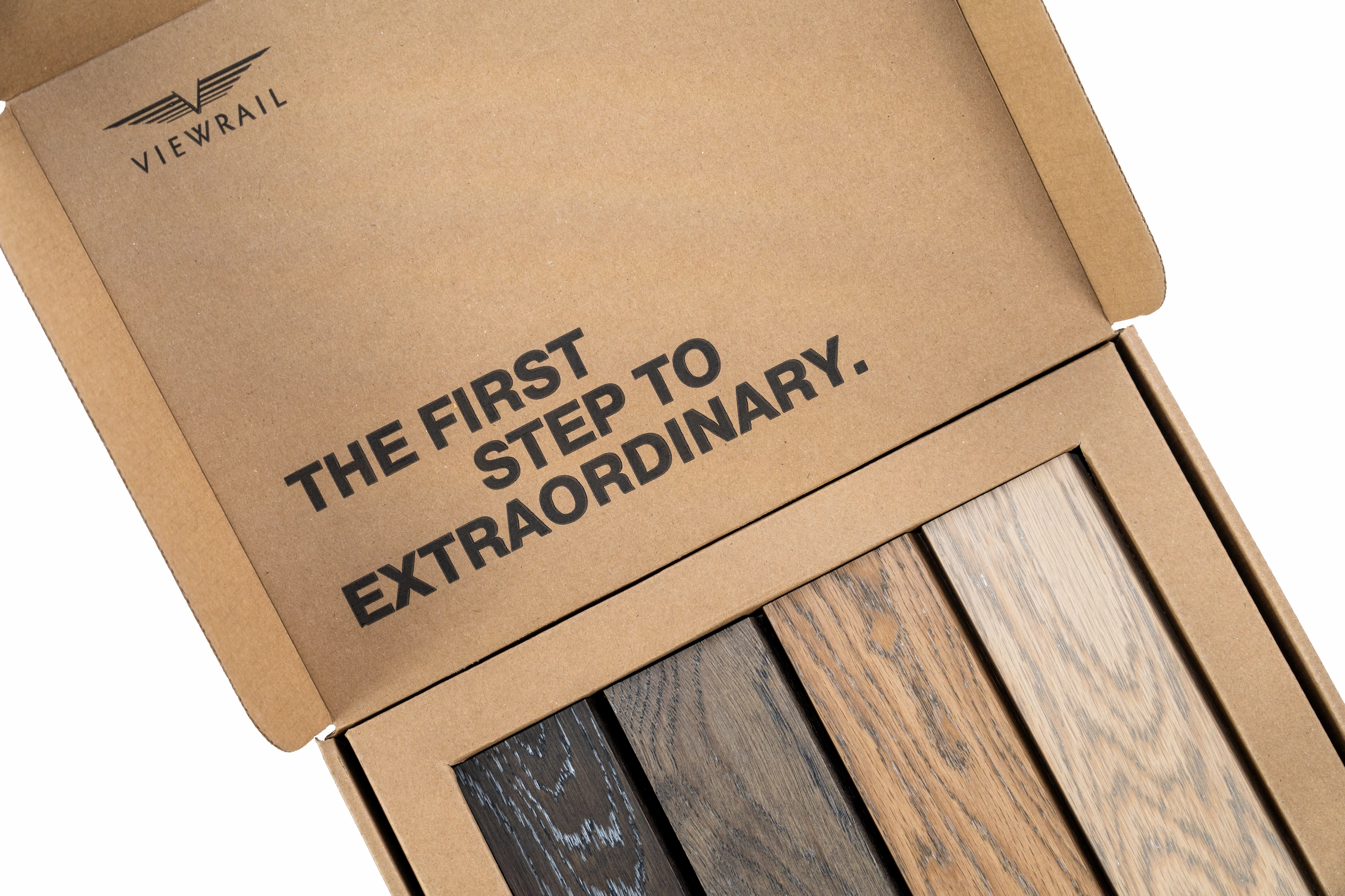 Open cardboard box with Viewrail logo and text "THE FIRST STEP TO EXTRAORDINARY." containing four wood samples in dark to light shades.