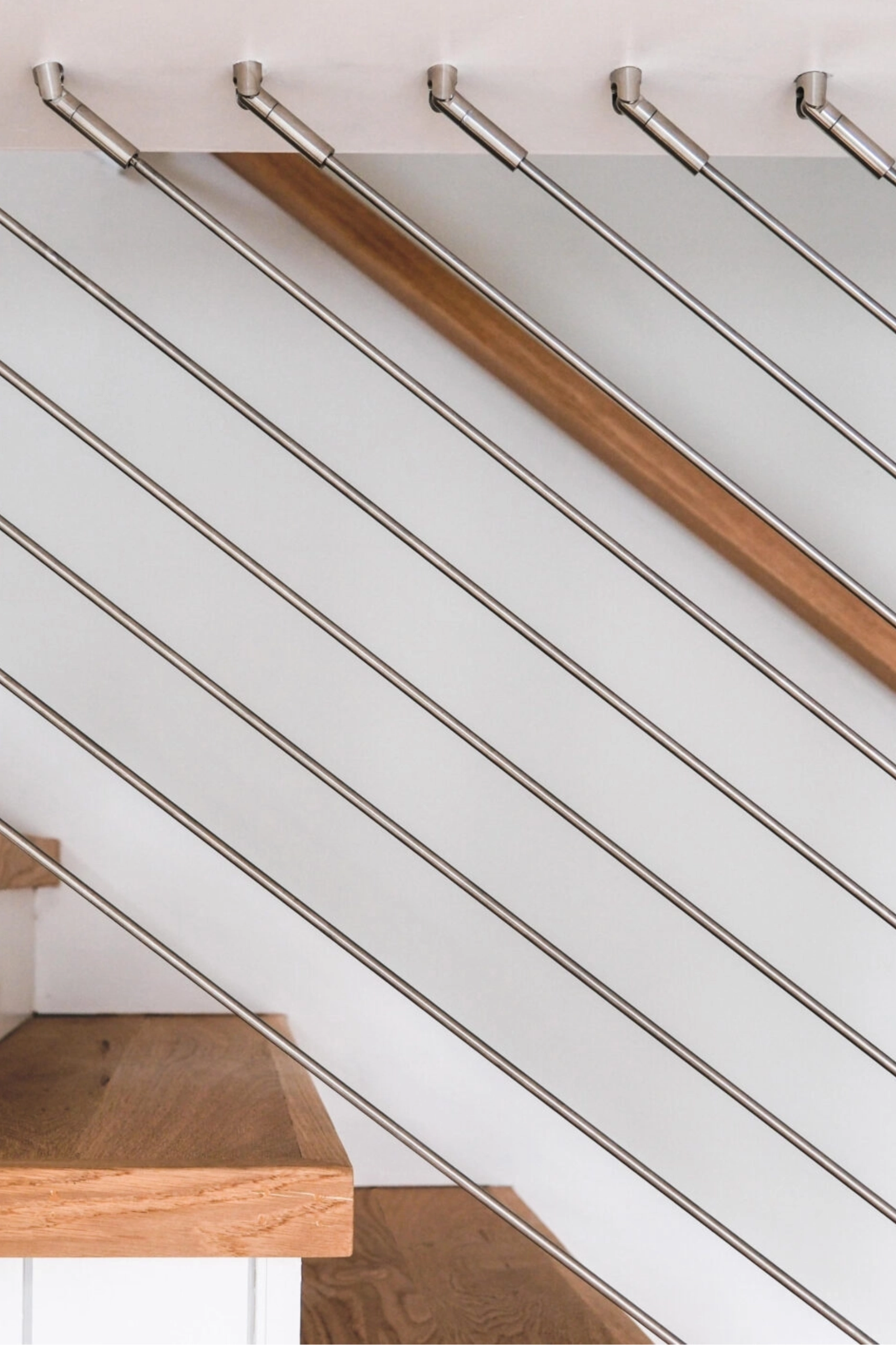 Stainless rods angle up into DriveTite fittings on a white stair rail, wood handrail behind