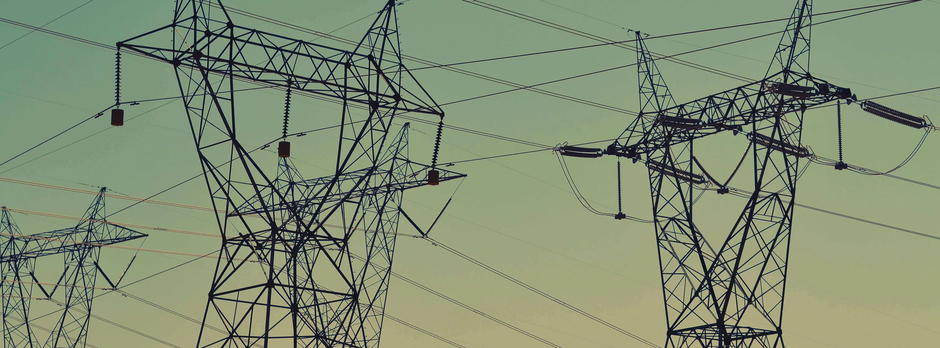 Silhouettes of electrical transmission towers and power lines against a clear dusk sky.
