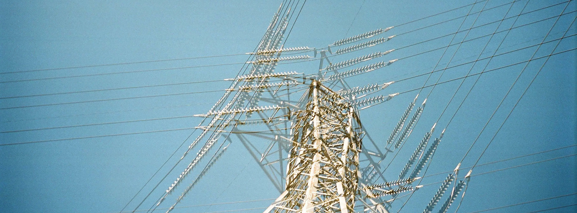 View looking up at a tall electricity transmission tower with power lines against a clear blue sky.
