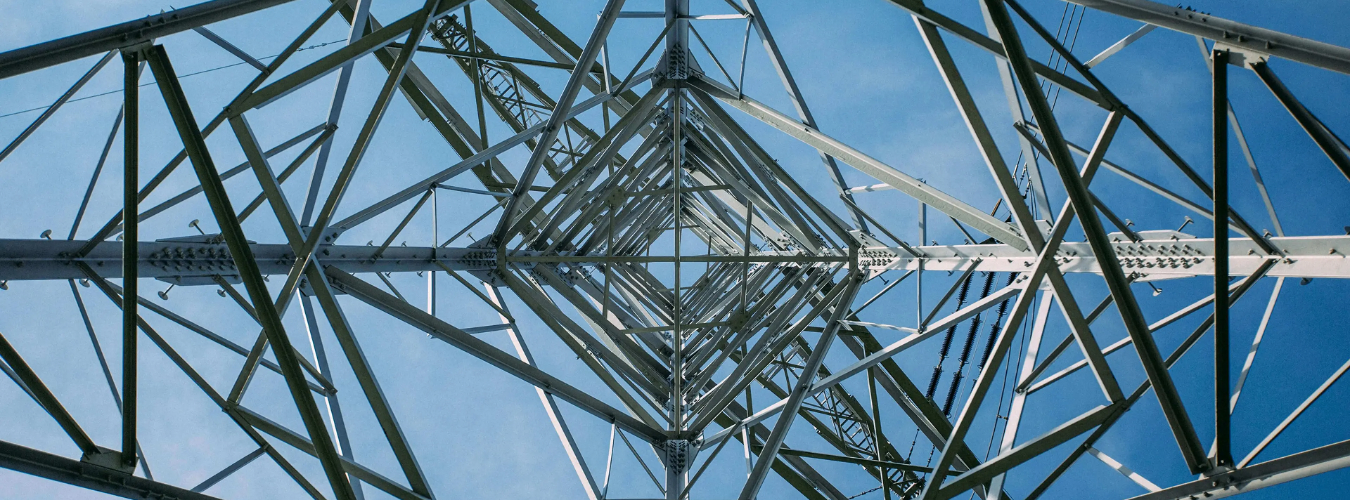 Looking up inside a steel electrical transmission tower against a clear blue sky.