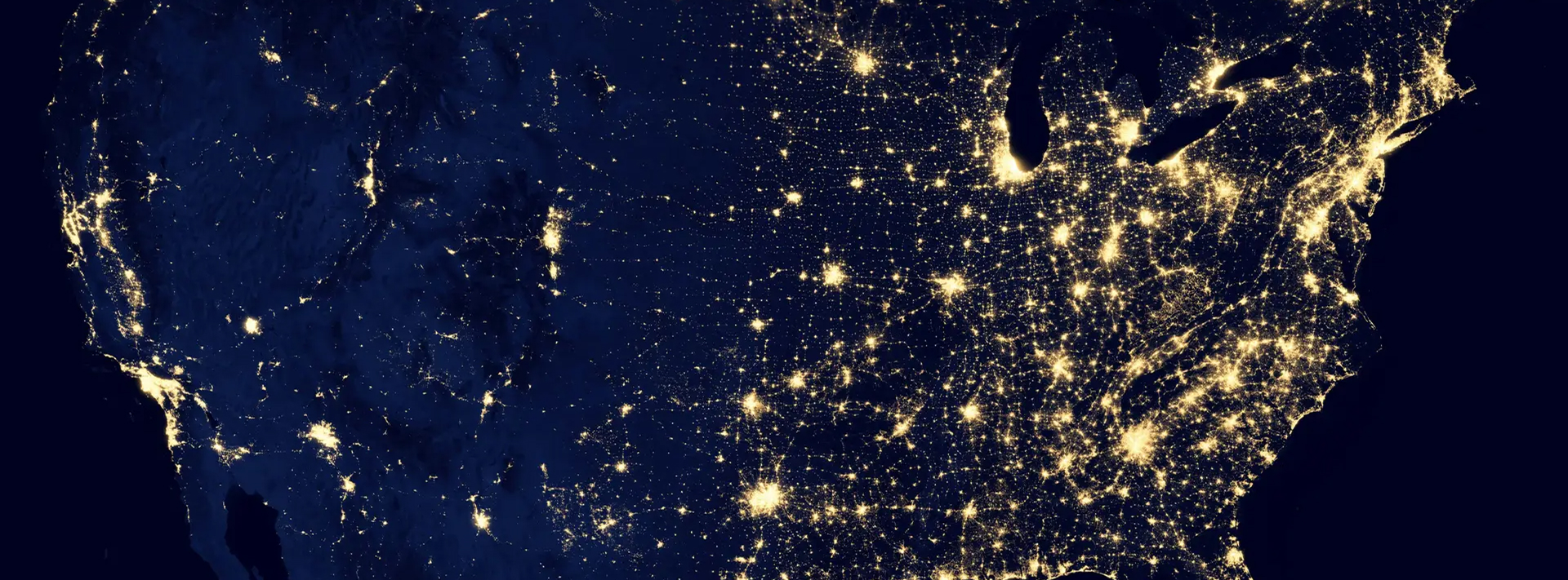 Satellite view of the US at night showing city lights concentrated in the east and west coasts.