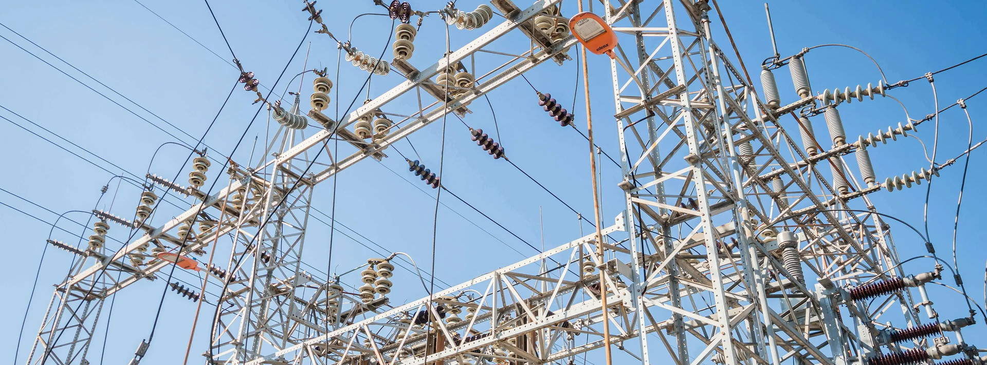 Metal electrical substation structure with insulators and wires against a clear blue sky.