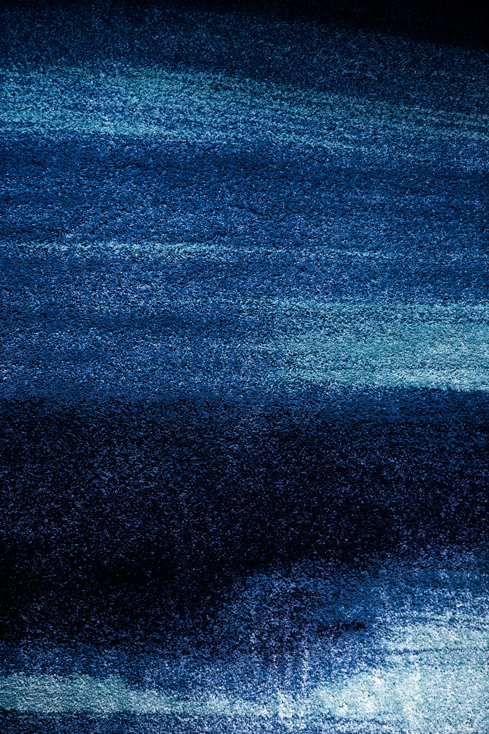 Texture en gros plan d'un tapis ou tissu avec des nuances de bleu allant du bleu clair au bleu foncé formant des lignes horizontales floues.