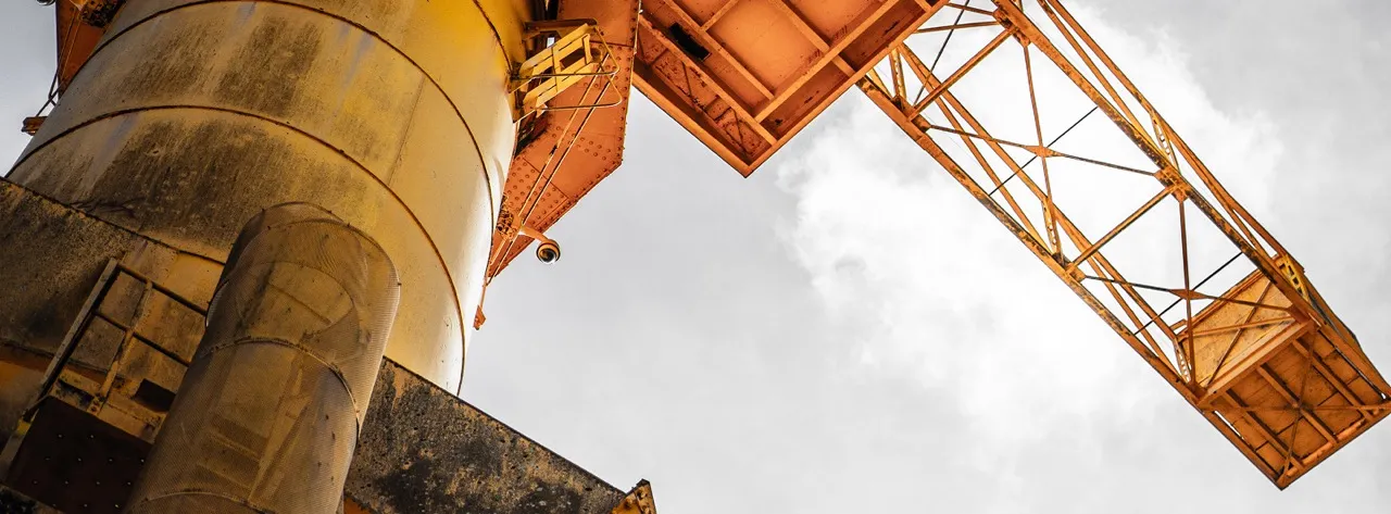 Vue en contre-plongée d'une structure industrielle jaune rouillée avec des poutres métalliques et un ciel nuageux en arrière-plan.