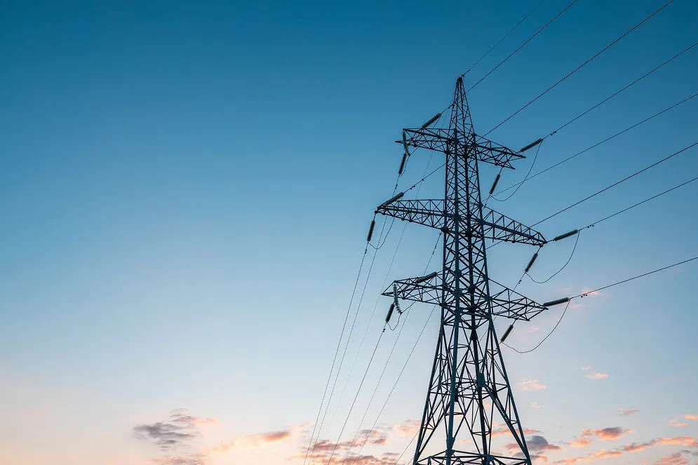 Un pylône électrique métallique soutenant plusieurs lignes haute tension contre un ciel clair au crépuscule avec quelques nuages rose pâle.