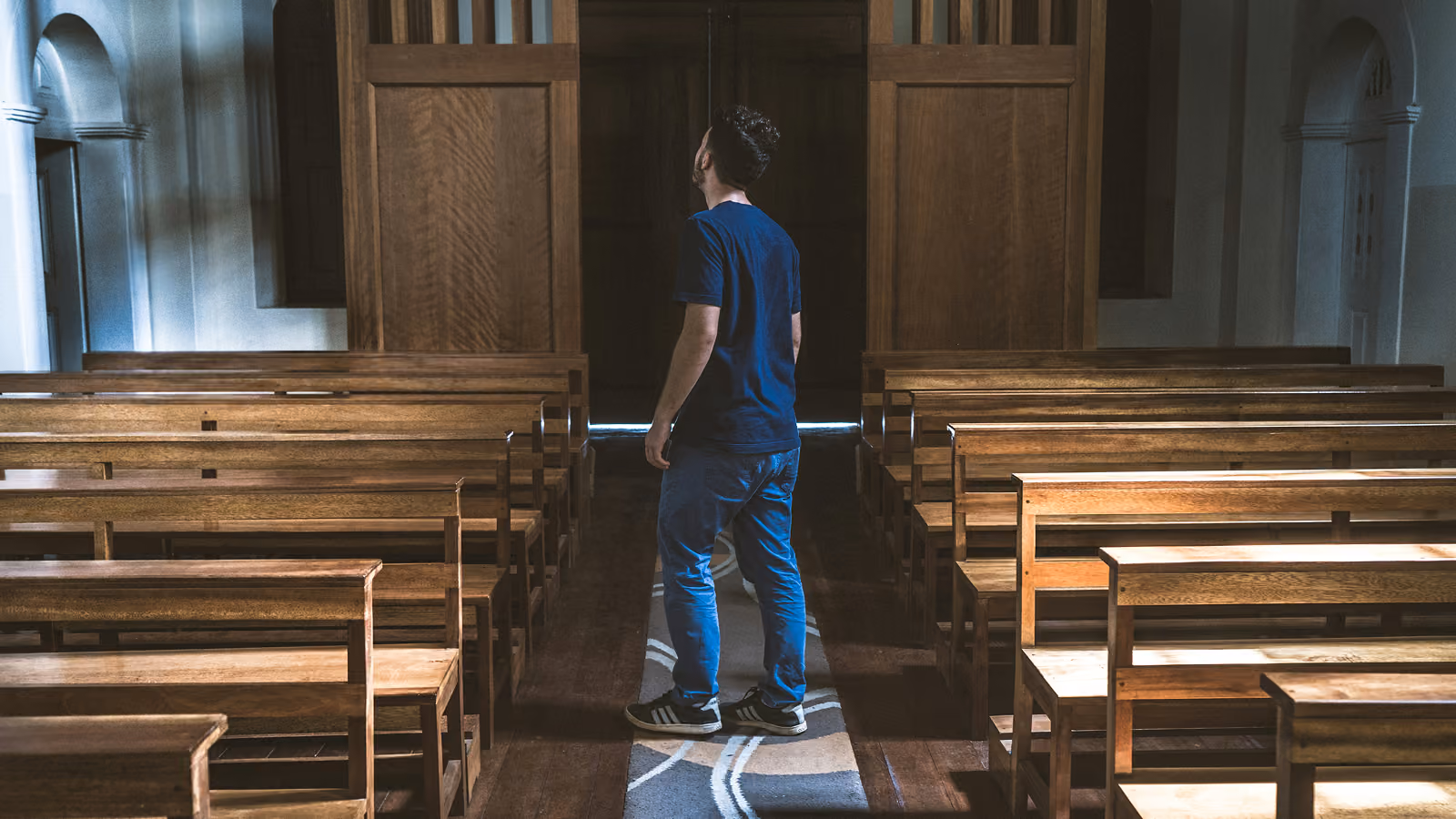 A young man standing in an aisle with benches on either side.