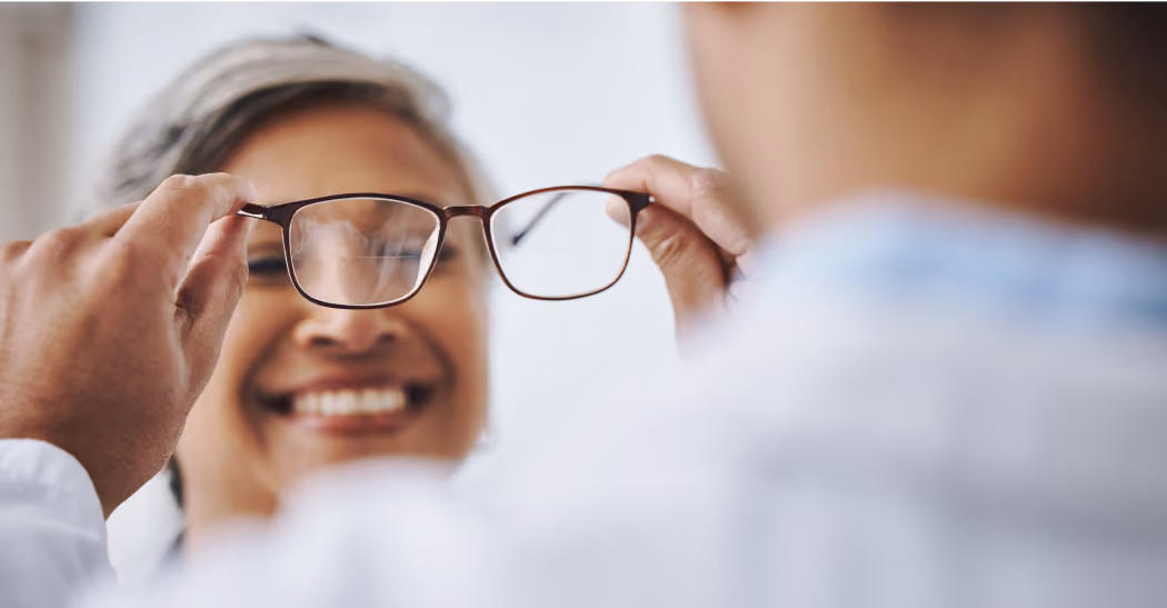 Person smiling while another holds glasses in front of them during an eye exam.