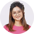 Portrait of a woman with glasses and long brown hair smiling, wearing a pink top.