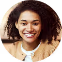 Smiling woman with curly hair wearing a beige sweater and white top.