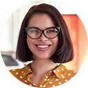 Smiling woman with short brown hair, glasses, and yellow polka-dot blouse in a bright office.