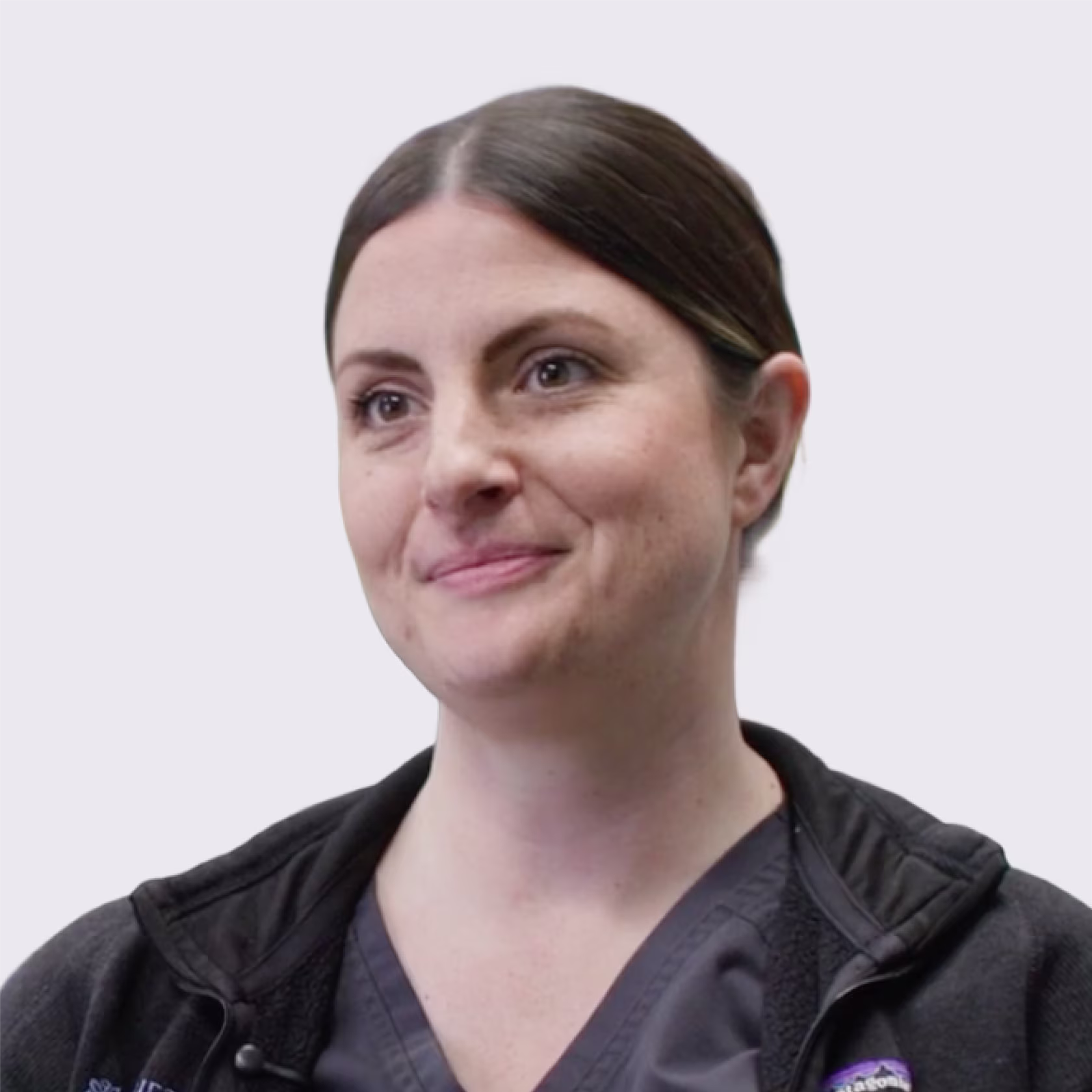 Portrait of a woman with dark hair tied back, wearing a dark medical scrub and jacket, smiling slightly.