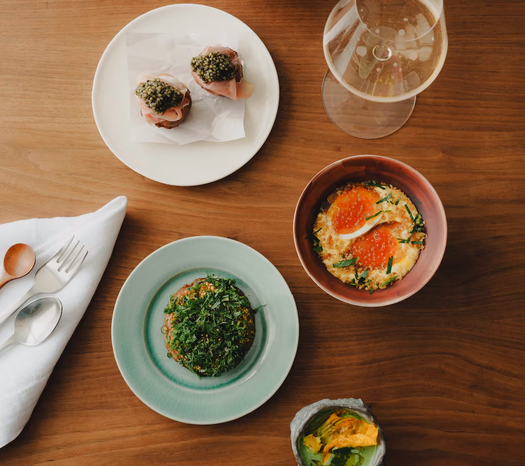 Overhead spread of Bionic Lunch dishes with caviar, salmon roe, fresh herbs and a glass of Champagne