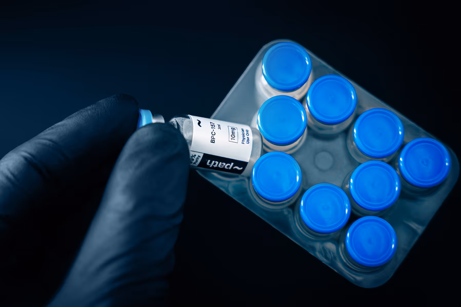 Gloved hand holding a vial labeled 10mg among a tray of vials with blue caps.