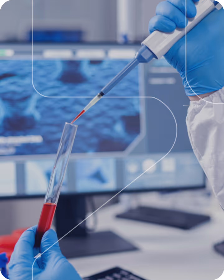 Gloved hands using a pipette to draw red liquid into a test tube in a lab with a screen background.