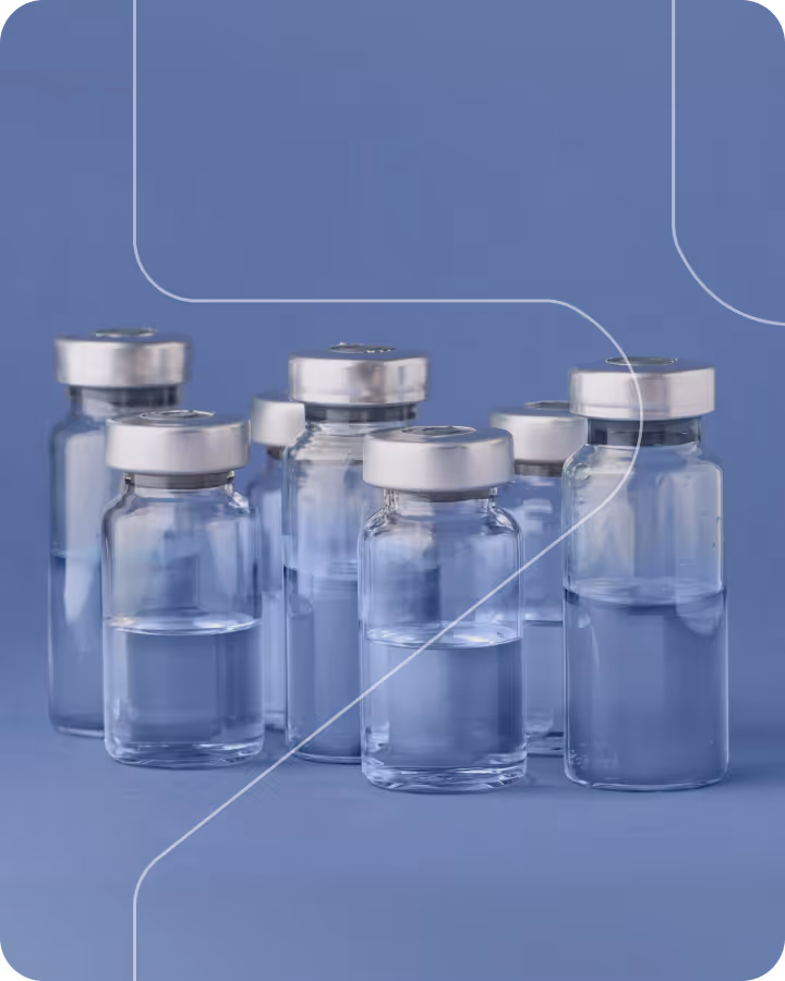 Group of clear glass vials with silver caps, some filled with liquid against a blue background.