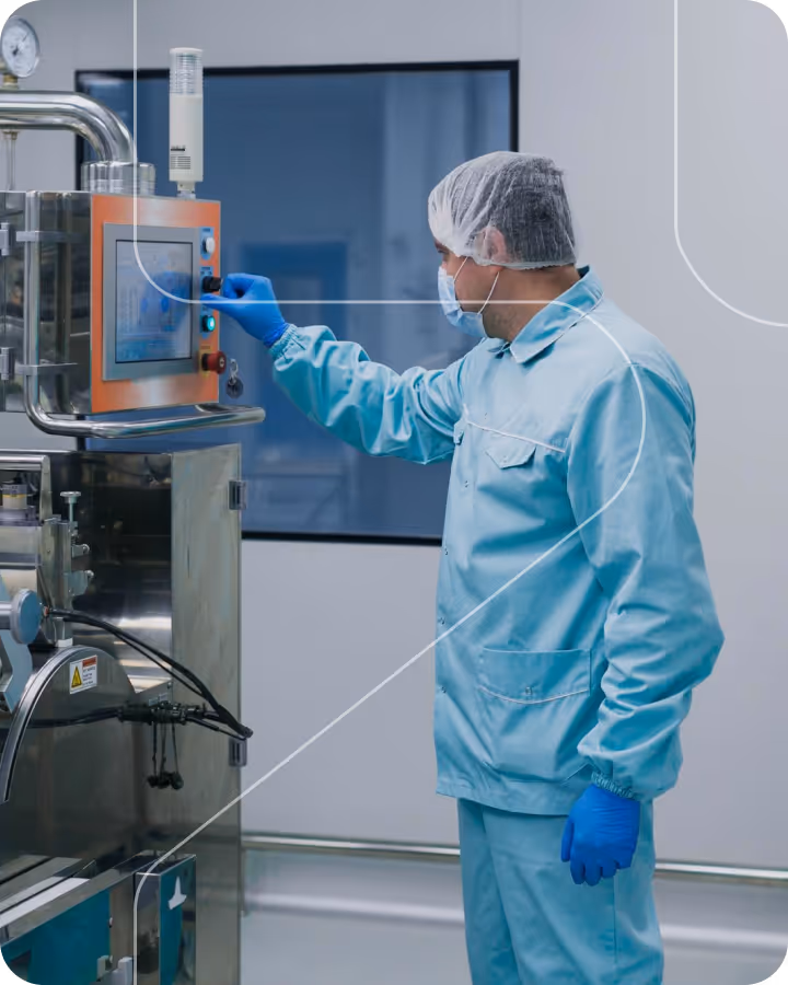 Worker in protective clothing operating control panel on industrial machine in sterile environment.
