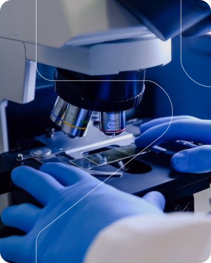 Gloved hands adjusting a slide under a microscope lens in a laboratory setting.