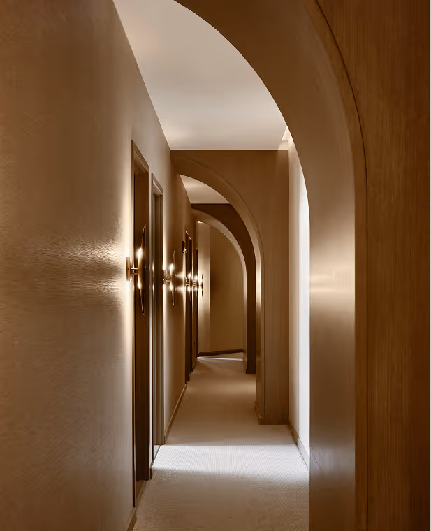 Corridor with repeating archways and wall lights casting warm shadows in a beige interior.