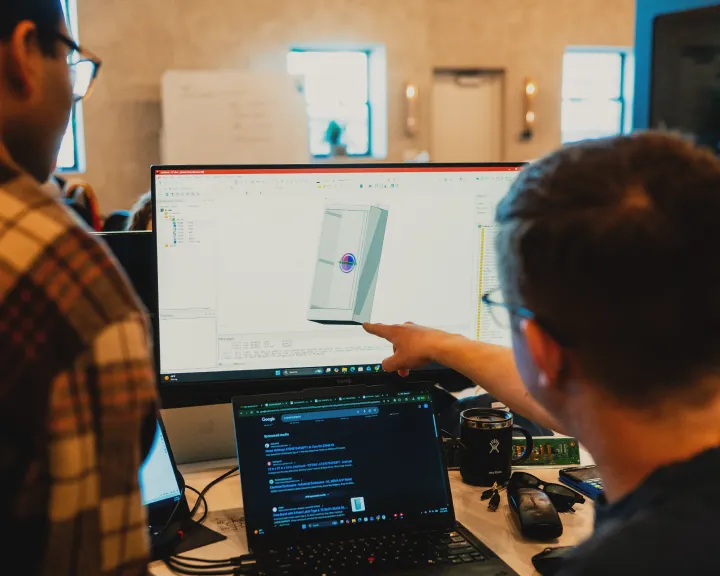 Engineers reviewing a 3D CAD model of a control panel enclosure in design software on a desktop monitor.