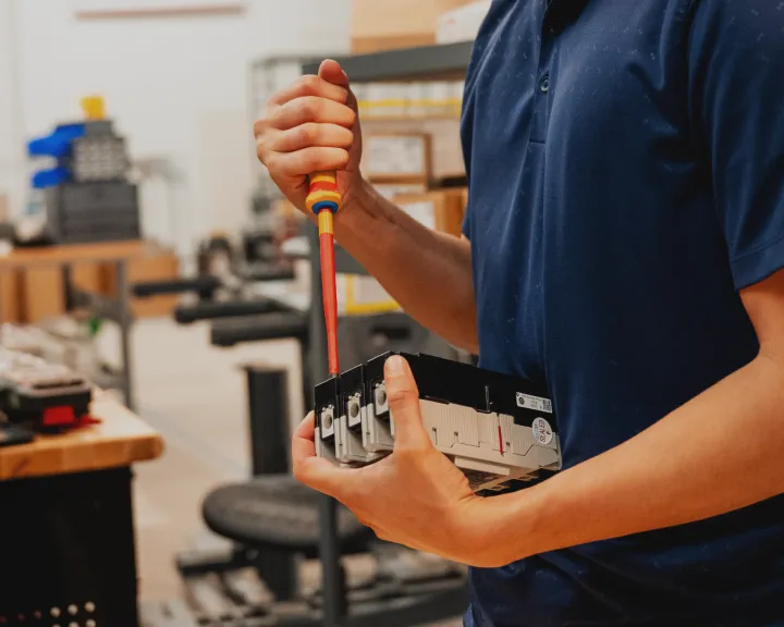 Technician using an insulated screwdriver to assemble a circuit breaker for a control panel build.