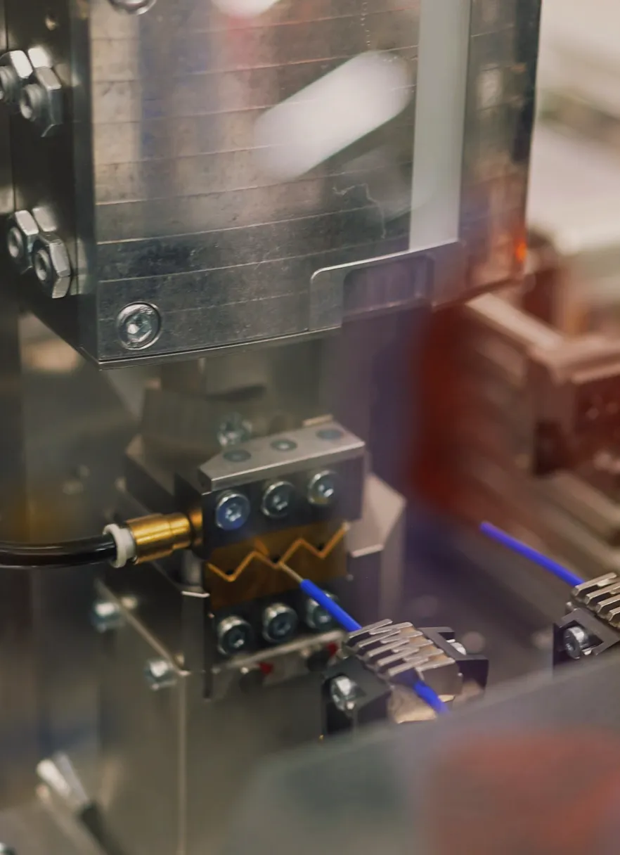 Automated wire-processing machine cutting, stripping, and routing blue control wiring for control panel assembly.