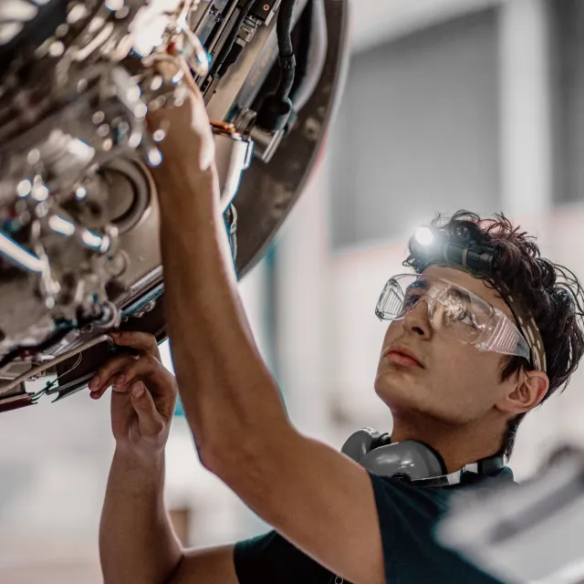 Engineer in safety glasses and a headlamp inspecting precision machinery in an advanced manufacturing facility.