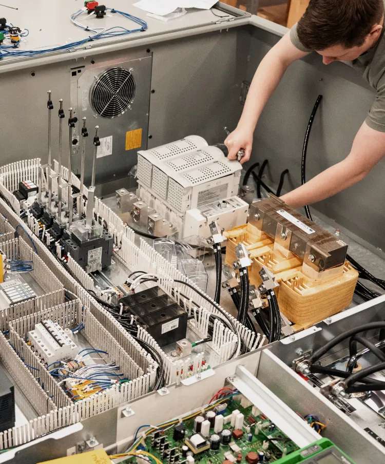 Technician assembling a control panel with a transformer, power supply, circuit breakers, and wire ducts.