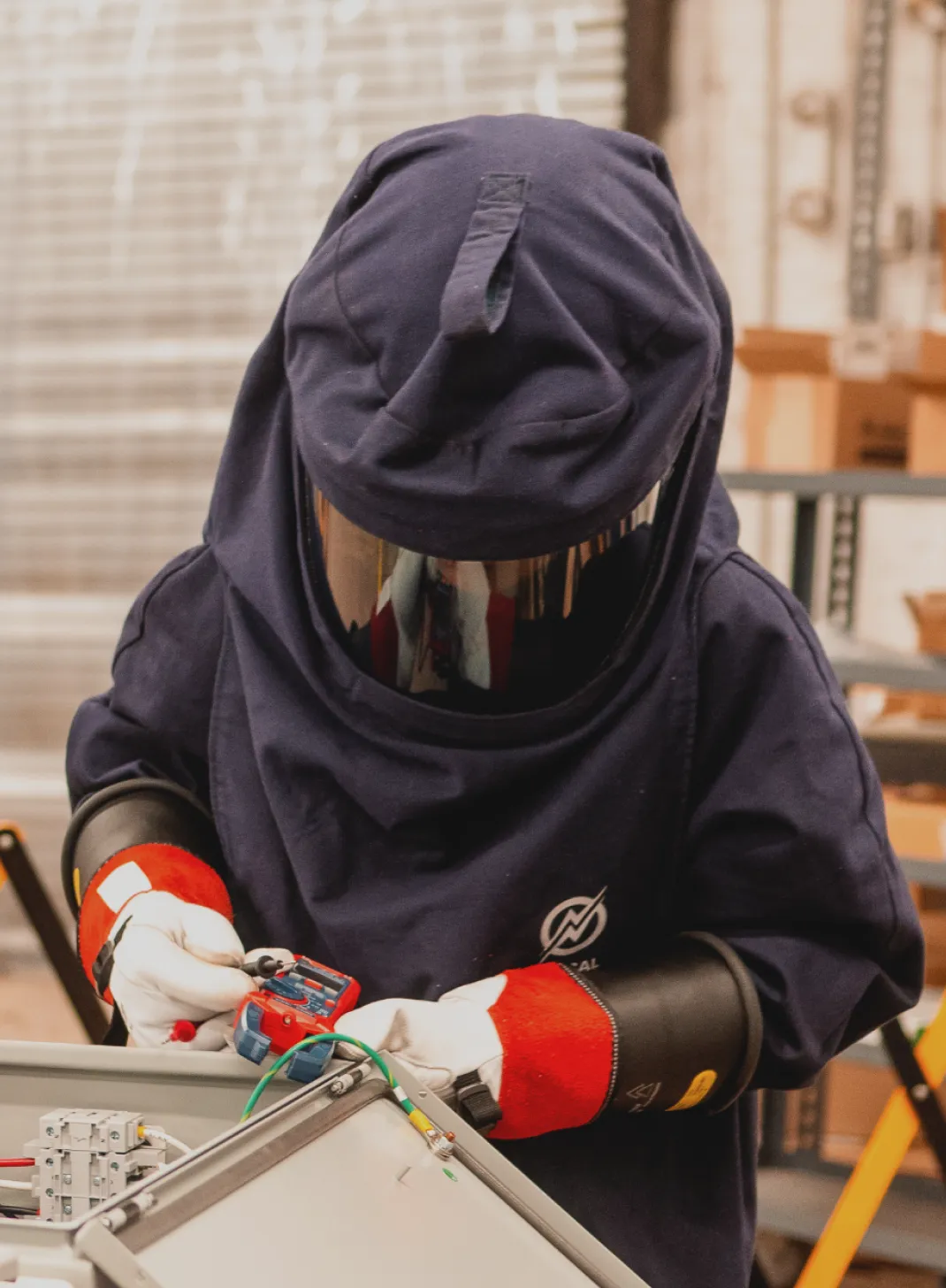 Technician in arc-flash gear stripping color-coded wires into DIN-rail terminal blocks inside a control panel enclosure.