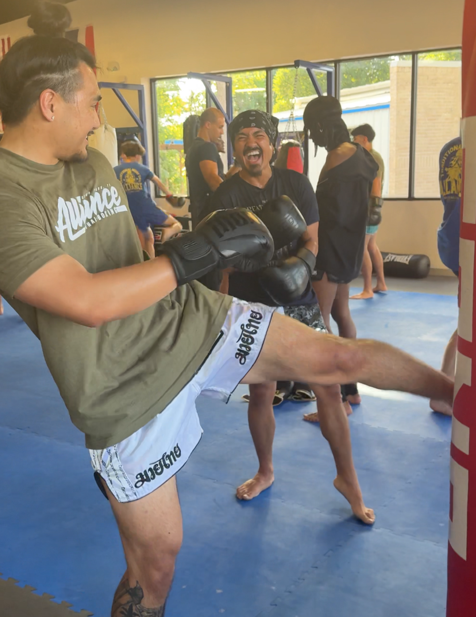 Members laughing while kicking the heavy bag in a Basics Muay Thai class at Alliance Thai Boxing Academy