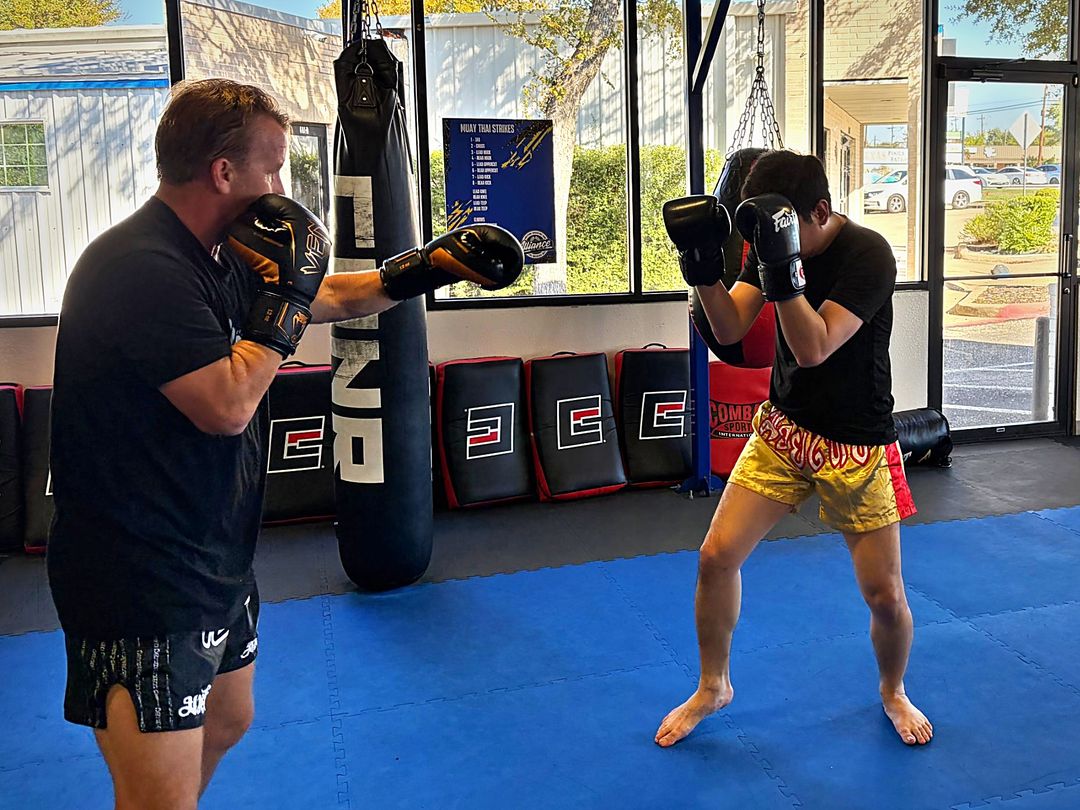 Boxer throwing a jab while his partner holds a high guard in boxing class at Alliance Thai Boxing Academy in Cedar Park, TX