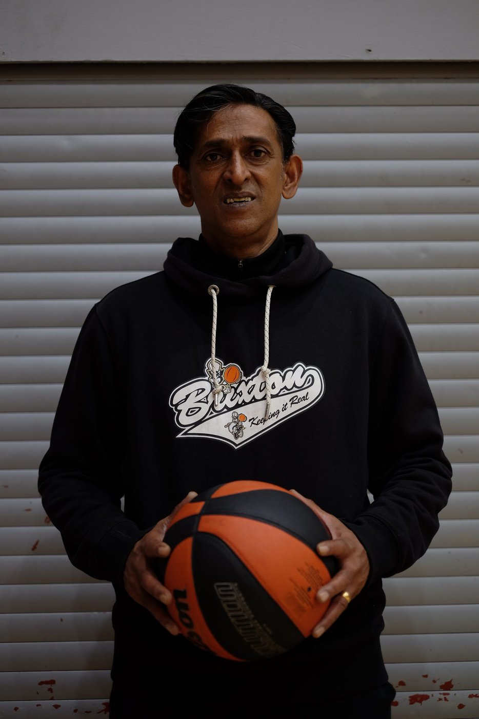 Coach Saivy holding a basketball in a Brixton Topcats hoodie