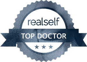 A circular badge with the text 'realself' at the top and 'TOP DOCTOR' at the center, surrounded by five stars beneath the text.