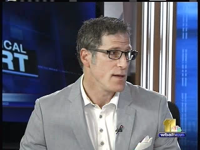 A man with glasses wearing a light gray suit jacket and a white shirt, speaking during a television broadcast. The lower right corner features the 'WBAL' logo in yellow and blue with the number '11' in white.