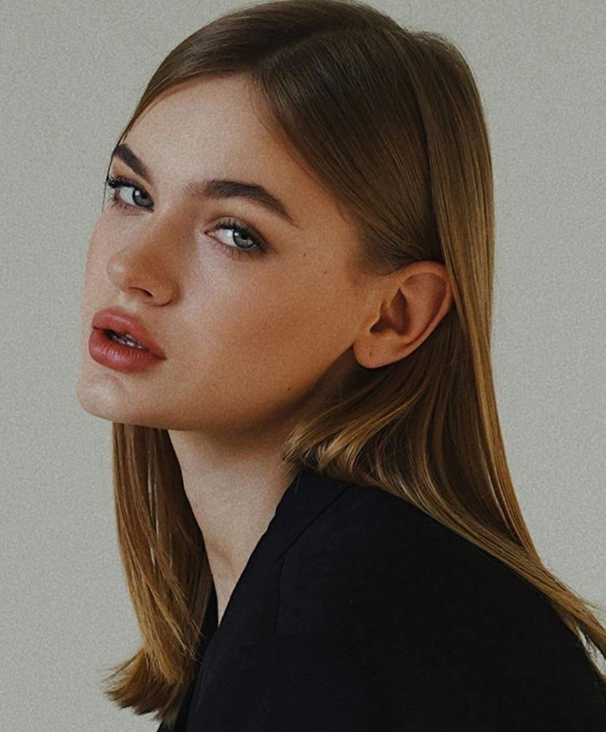 A portrait of a young woman with shoulder-length straight hair, wearing a black top, gazing sideways with a soft expression. Her lips are slightly parted and her skin has a natural glow.